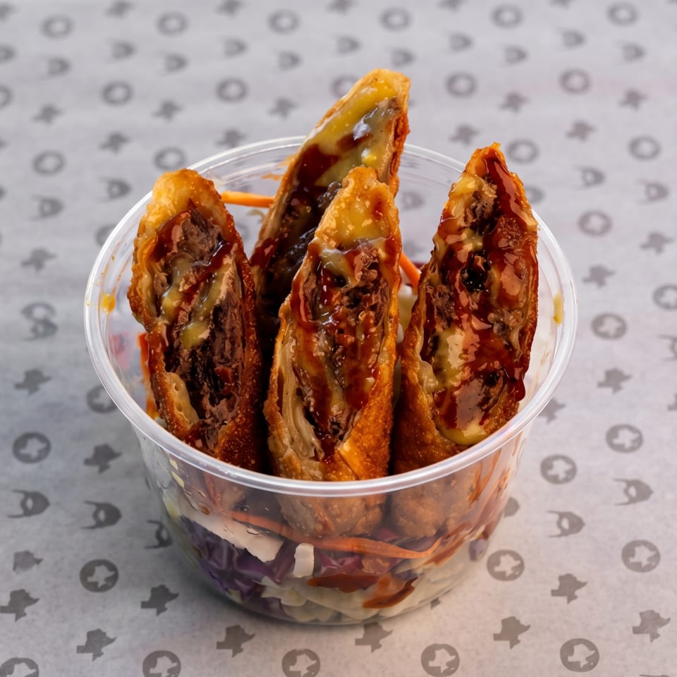 Crispy stuffed tacos drizzled with sauce in a clear plastic cup on patterned paper.