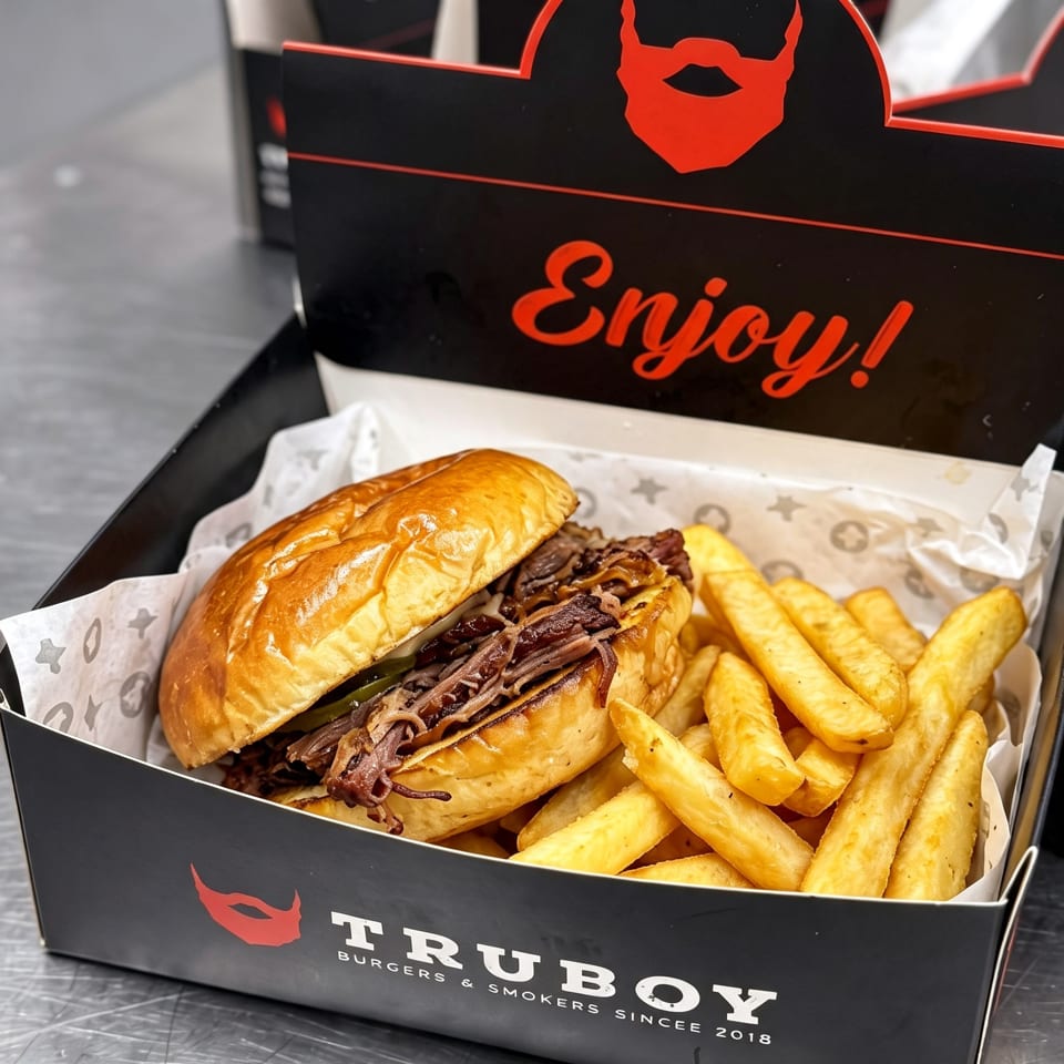Pulled beef burger with caramelized onions and thick-cut fries served in a branded Truboy box.