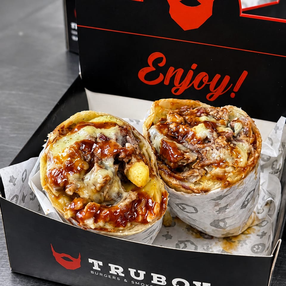 Two loaded, sauce-covered burgers with melted cheese and fries in a branded Truby Burgers & Smokers takeaway box.