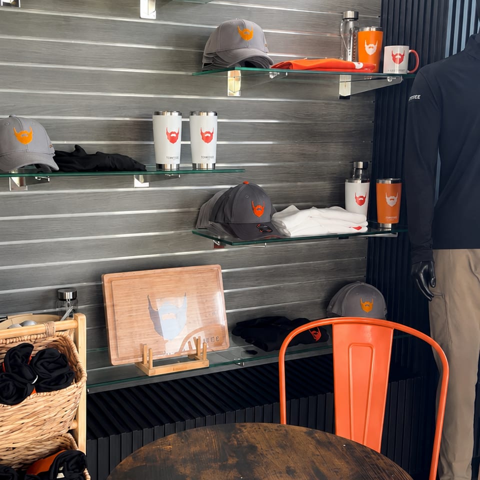 Restaurant merchandise display with branded tumblers, caps, clothing, a mannequin, and an orange chair around a wooden table.