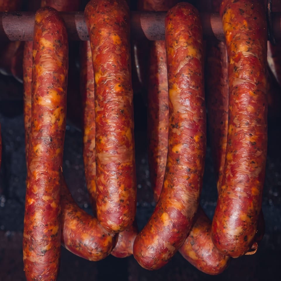 Rows of glossy, seasoned sausages cooking on a dark metal grill.